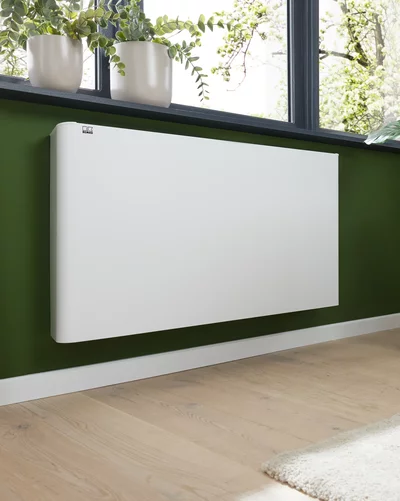 Weißer elektrischer Flächenstrahler von Remko an einer grünen Wand unter einem Fenster.